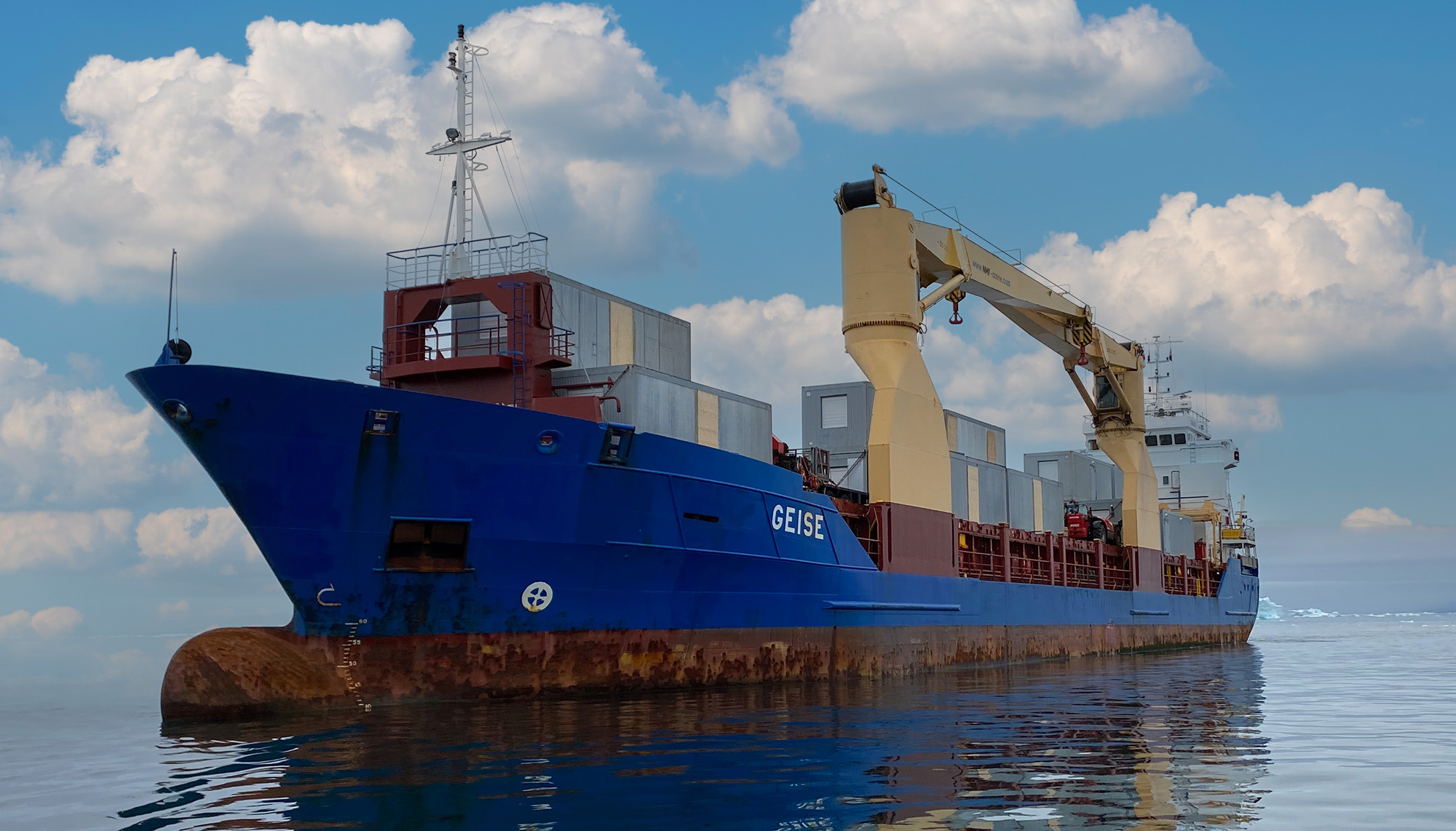 Blue cargo ship named 'GEISE' on calm waters, equipped with a large crane and containers on its deck, under a partly cloudy sky.